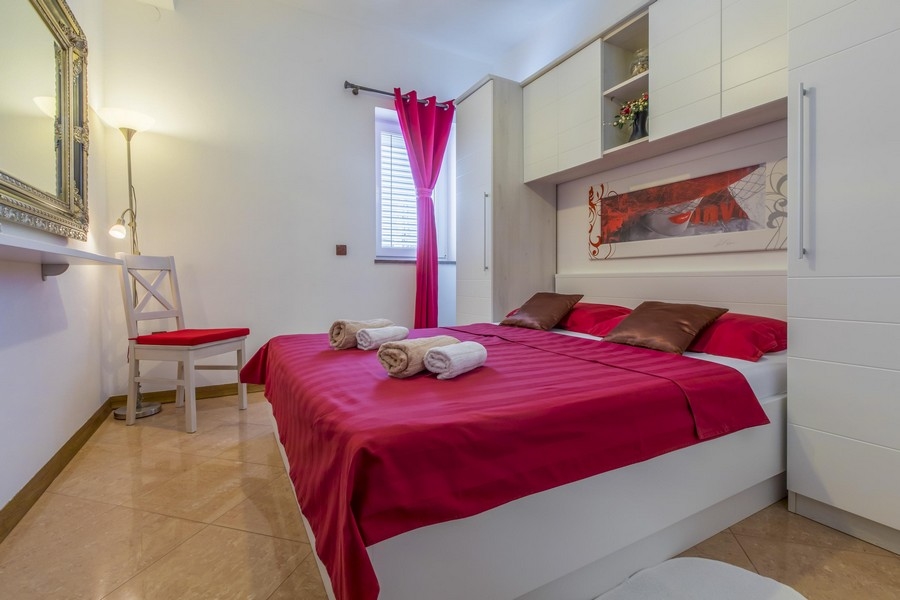 Schlafzimmer mit rotem Bettbezug und weißem Mobiliar in einem kroatischen Mehrparteienhaus am Meer