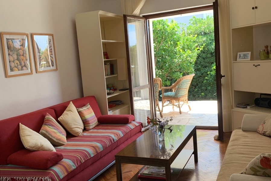 Wohnzimmer mit offener Tür zur Terrasse, rotem Sofa und Blick ins Grüne des Hauses in Kroatien