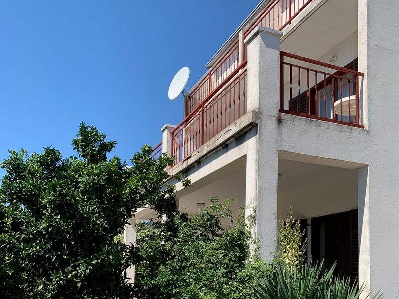 Vorderansicht des zu verkaufenden Hauses in Kroatien mit Balkon und Schatten spendenden Bäumen