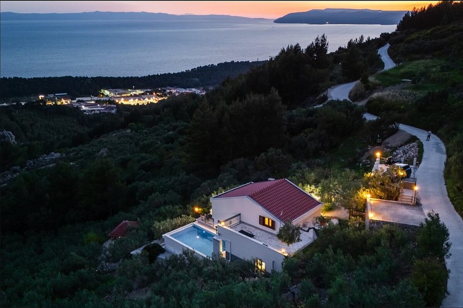 Villa am Hang mit beleuchtetem Pool am Abend