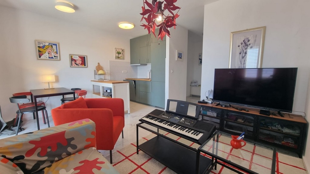 Wohnbereich mit TV-Ecke und Blick in die moderne und kleine Küche.