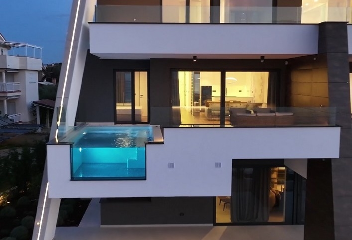 Moderne Meerfront-Immobilie in Kroatien bei Dämmerung mit beleuchtetem Infinity-Pool und mehrstöckiger Fassade.