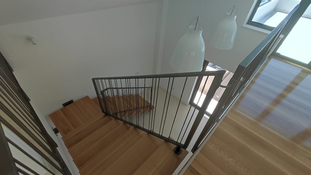 Penthouse kaufen Kroatien - Innenansicht eines eleganten Penthouses mit Holztreppe und Designer-Hängeleuchten, mit Blick auf den Wohnraum unten, angeboten von Panorama Scouting.
